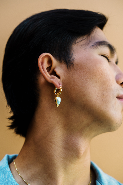 Close-up of a man showcasing the Fireball Pearl Charm, a bold South Sea pearl in a fireball shape, attached to a gold hoop earring. This charm-only piece can be paired with our 'MATAHARI' hoop earrings (sold separately) or also be worn as a pendant for versatile styling.