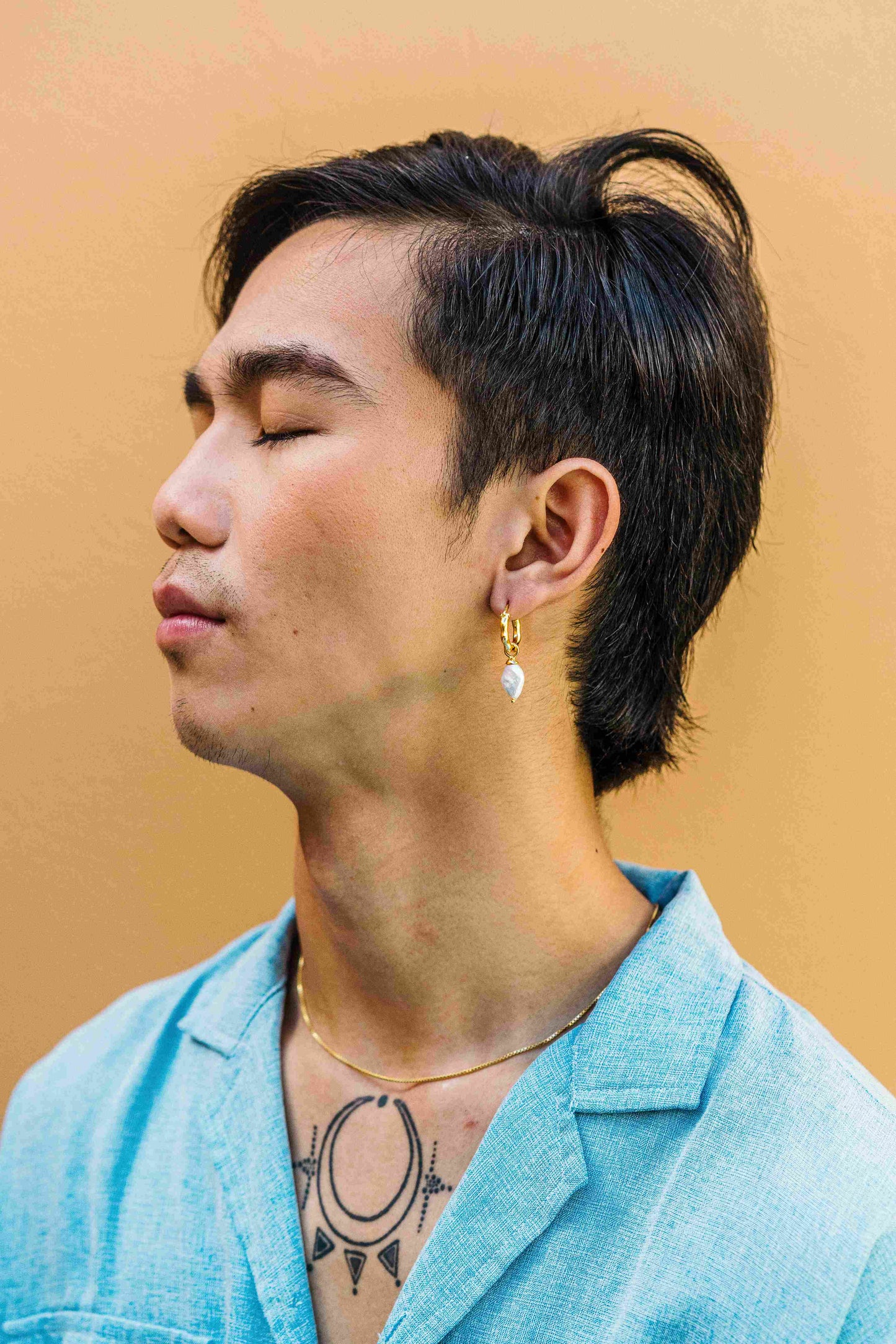 Male model showcasing the 'DIAMOND' charm with a diamond-shaped white freshwater pearl, worn on a gold hoop earring. This unisex pearl charm can slide onto hoop earrings or be used as a necklace pendant.