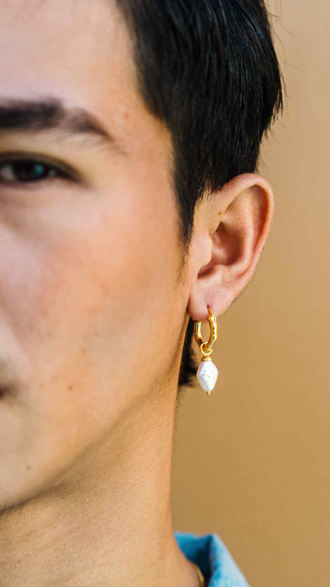 Close-up of a man wearing the 'DIAMOND' charm, featuring a white diamond-shaped freshwater pearl on a gold hoop earring. This versatile unisex pearl charm can also be styled as a pendant, offering multiple ways to wear.