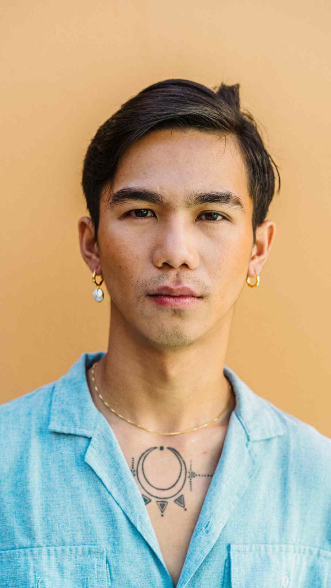 Profile shot of male model wearing chunky gold hoop earrings with one cereal charm on the left side. 