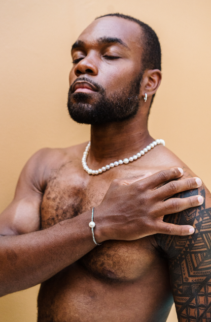 Man wearing South Sea and Freshwater Pearl necklace, with hand over his chest. He wears this pearl necklace and pairs it with a 925 Sterling Silver Dragon Bone bracelet with one South Sea Pearl and 925 Sterling Silver chunky hoop earrings. 