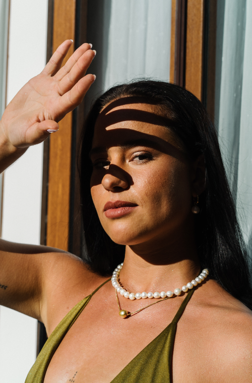 Woman with a green bikini top is holding her hand up to block the sun from her eyes wears a South Sea and Freshwater Pearl Mix Necklace and layers it with a single golden South Sea Floating pearl necklace on a gold vermeil chain.