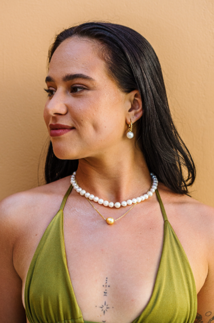 Profile shot of a woman in a green bikini  wearing a South Sea and Freshwater Pearl Mix Necklace and layers it with a single golden South Sea Floating pearl necklace on a gold vermeil chain. She is also wearing gold vermeil hoops with interchangeable White South Sea Peal Drop Charm earrings.