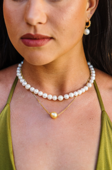 Close up of a woman's neckline in a green bikini  wearing a South Sea and Freshwater Pearl Mix Necklace and layers it with a single golden South Sea Floating pearl necklace on a gold vermeil chain. She is also wearing gold vermeil hoops with interchangeable White South Sea Peal Drop Charm earrings.