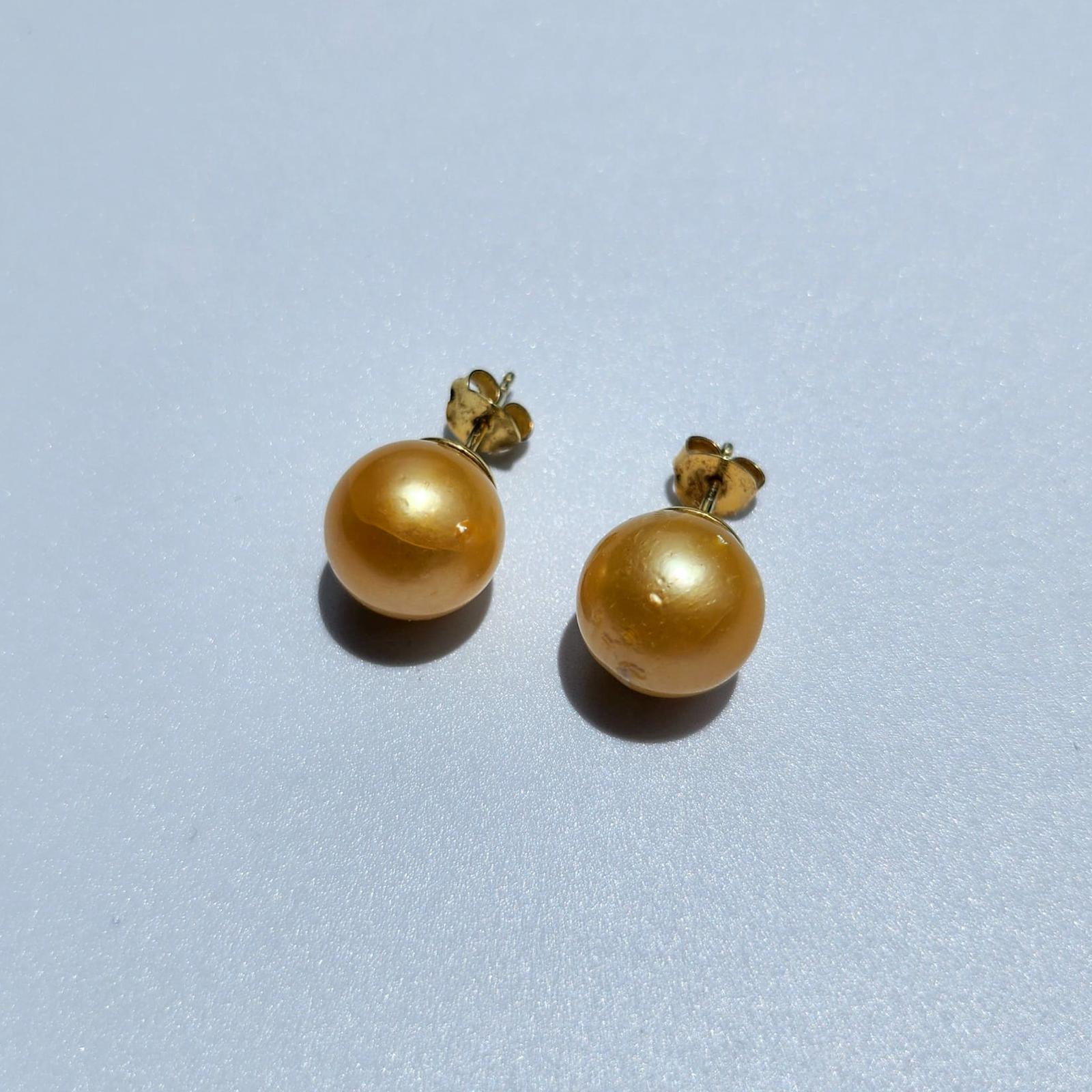 Close up of Golden yellow honey colored South Sea Pearl stud earrings set in 14k gold vermeil on white surface.