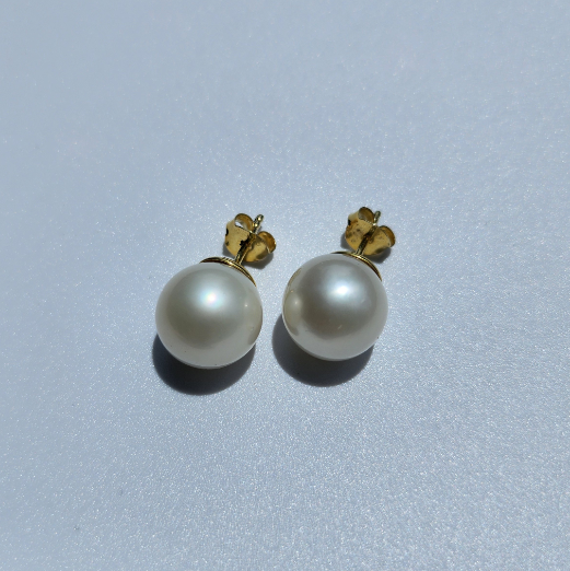 Close up of round white South Sea Pearl stud earrings with 14k Gold Vermeil setting on white background.