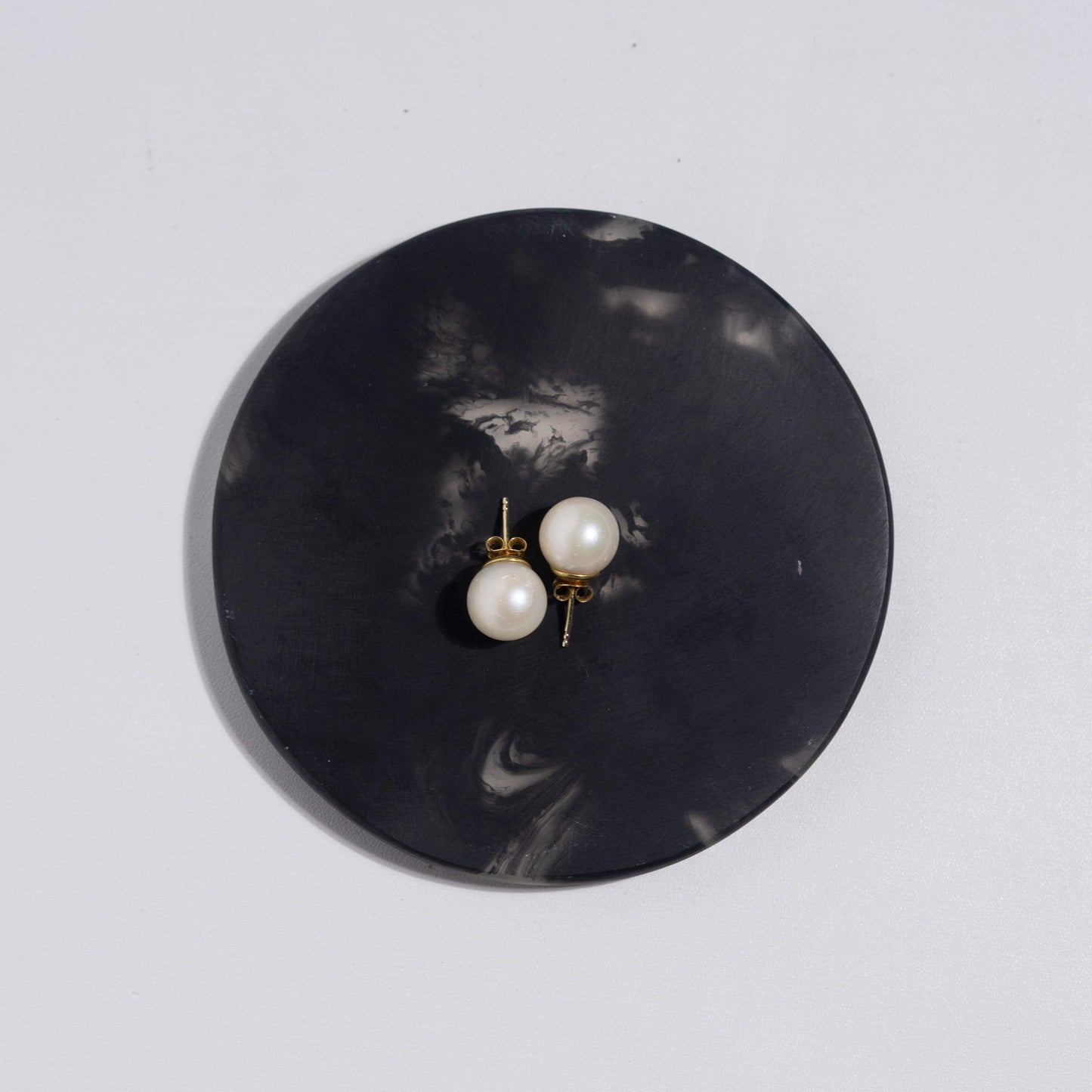 Close up of white South Sea Pearl Stud Earrings set in 14k Gold Vermeil sitting on round black display.